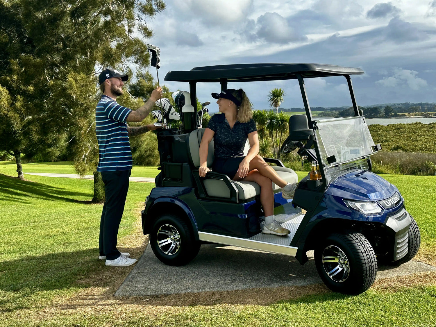A man putting a golf club back in his bag while a young woman sits in the Global Carts 2 Seater Golf Cart