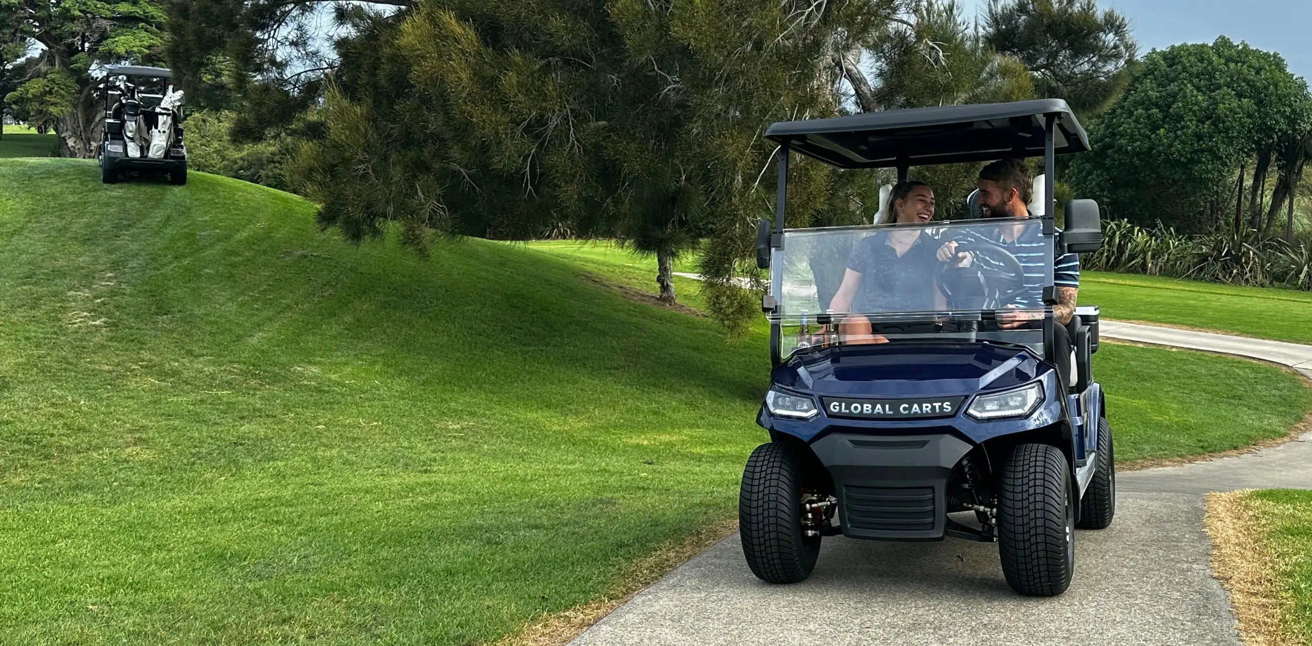 Two people sitting in a Global Carts electric golf cart on a golf course in New Zealand